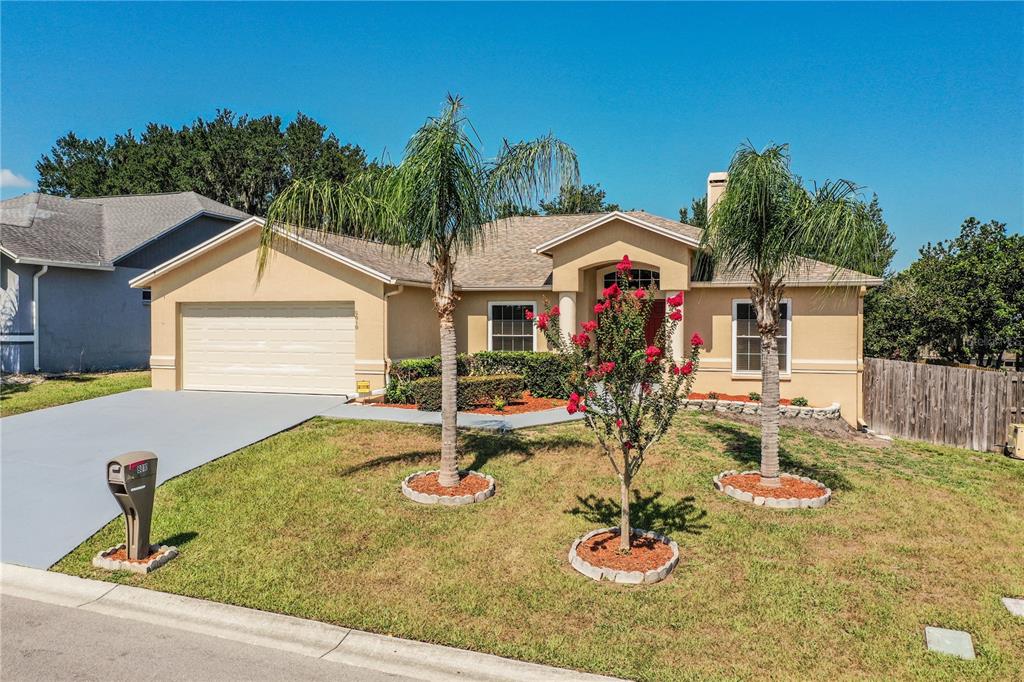 A single-story house with a beige stucco exterior, a two-car garage, and three palm trees — 8010 ASHLEY POINTE DRIVE, LAKELAND, FL