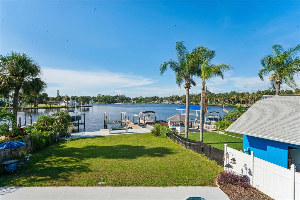 A grassy backyard leads to a private boat dock on a canal under a blue sky — 5531 MANATEE POINT DRIVE, NEW PORT RICHEY, FL