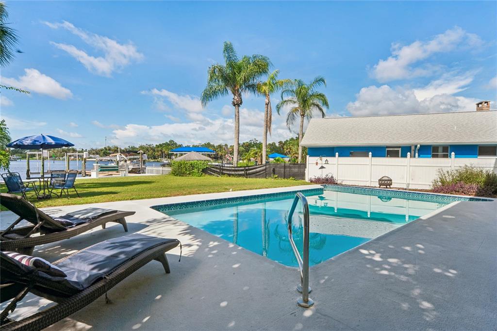 A backyard swimming pool with lounge chairs, a lawn, and a view of the water — 5531 MANATEE POINT DRIVE, NEW PORT RICHEY, FL