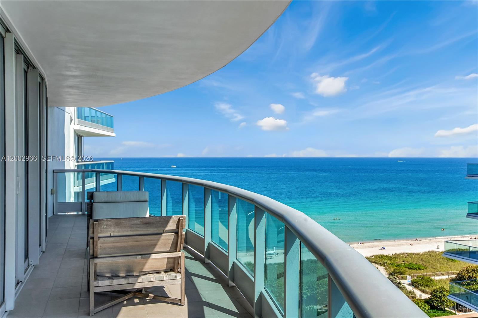 A balcony with a wooden chair overlooks the ocean and a sandy beach — 9401 Collins Ave # 1004, Surfside FL 33154, SURFSIDE, FL
