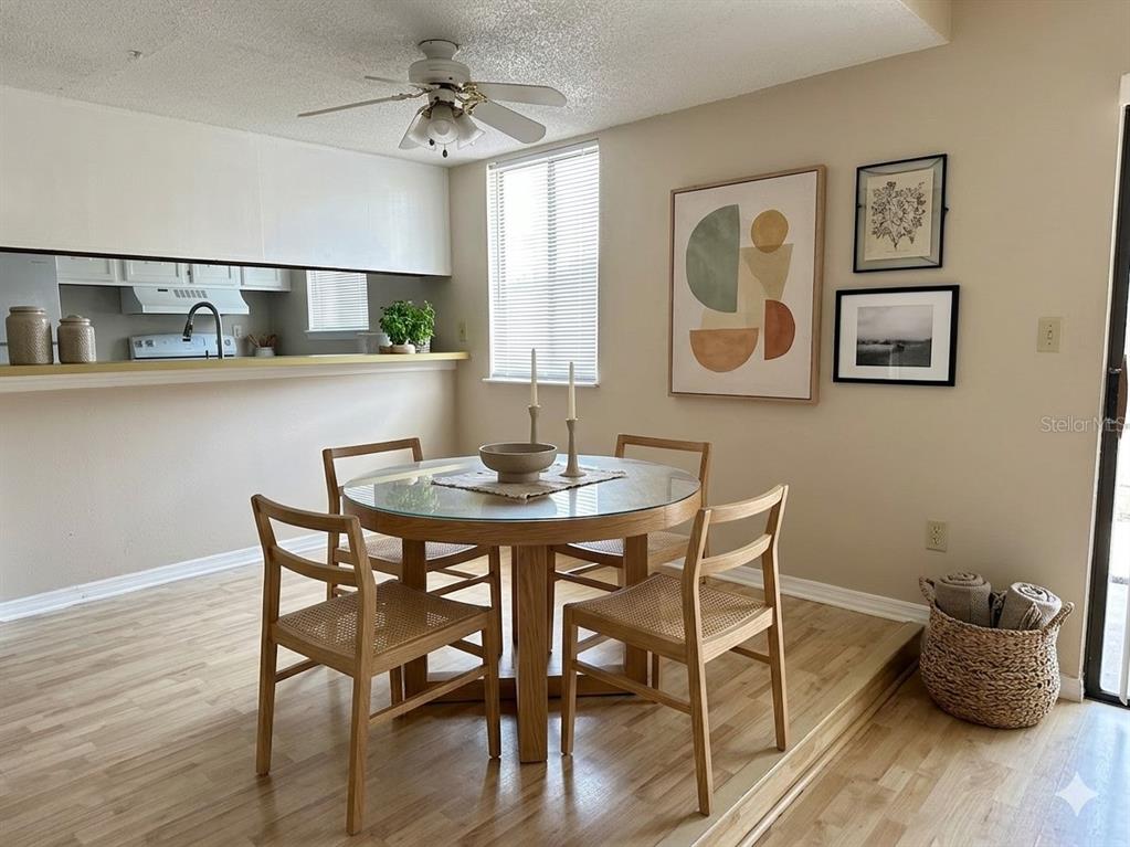 A dining area features a glass-topped wooden table, four chairs, and wall art on wood flooring — 1412 OAK PLACE UNIT J, APOPKA, FL