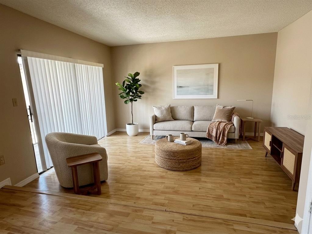 A living room features light wood flooring, a beige sofa, an armchair, and a round ottoman — 1412 OAK PLACE UNIT J, APOPKA, FL