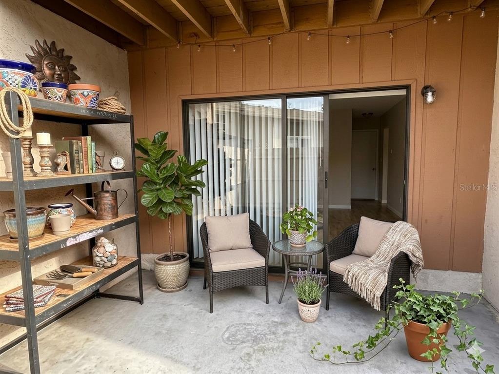 A covered patio features a metal shelving unit, two wicker chairs, and various potted plants — 1412 OAK PLACE UNIT J, APOPKA, FL
