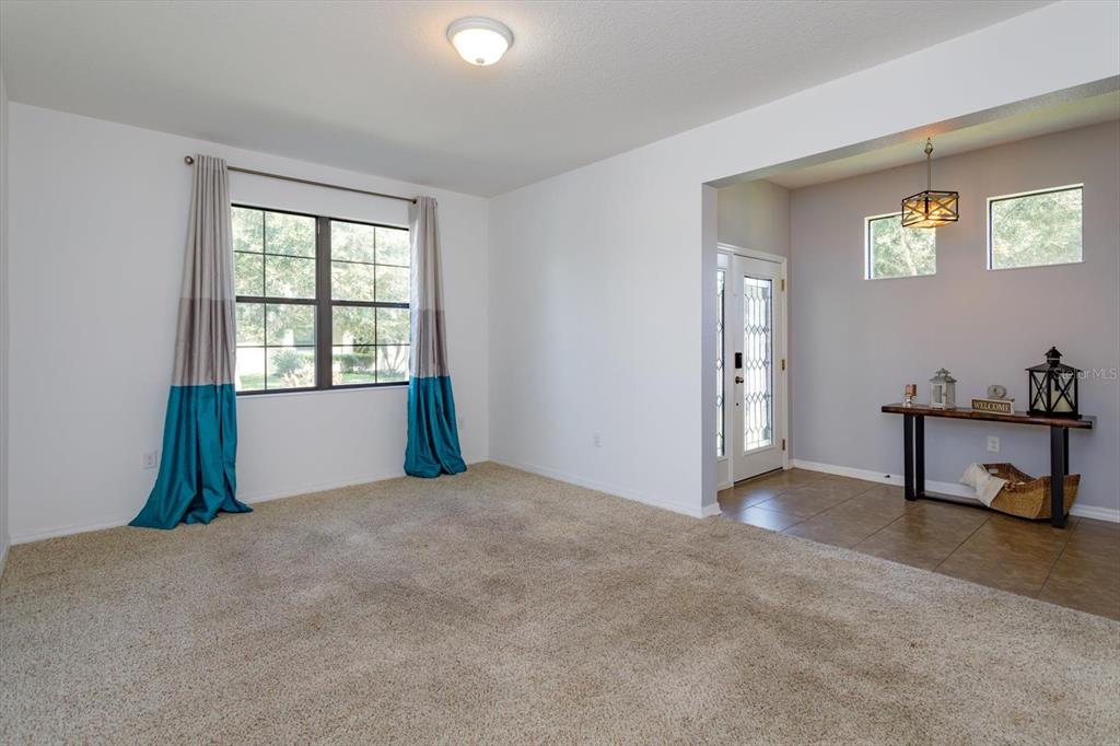 A carpeted living room with a window and an adjacent entryway featuring tiled flooring — 5106 APPENINE LOOP W, ST CLOUD, FL