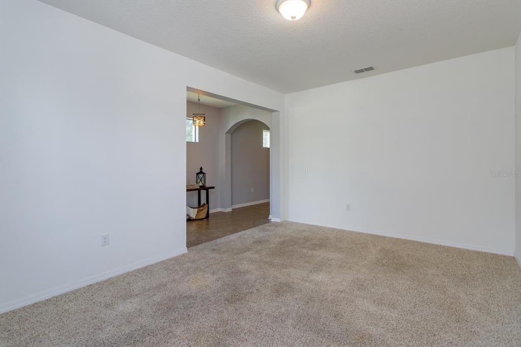 A carpeted room with white walls leads through an arched doorway into a tiled entryway — 5106 APPENINE LOOP W, ST CLOUD, FL