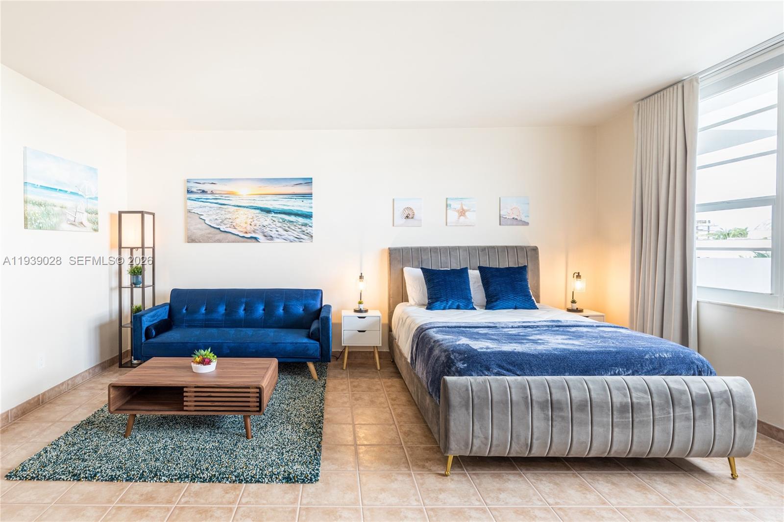 A studio apartment features a blue sofa, a gray upholstered bed, and tile flooring — 100 Lincoln Rd # 431, Miami Beach FL 33139, MIAMI BEACH, FL