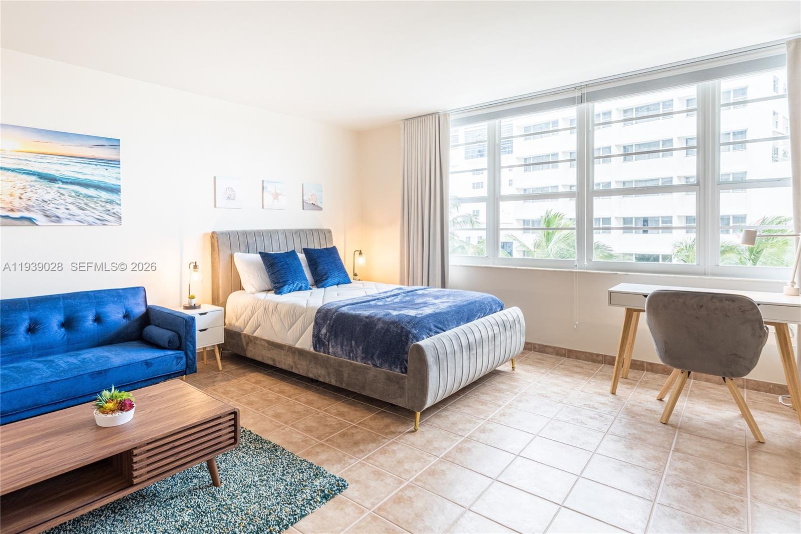 A bedroom features a gray upholstered bed, a blue sofa, and a desk by the window — 100 Lincoln Rd # 431, Miami Beach FL 33139, MIAMI BEACH, FL