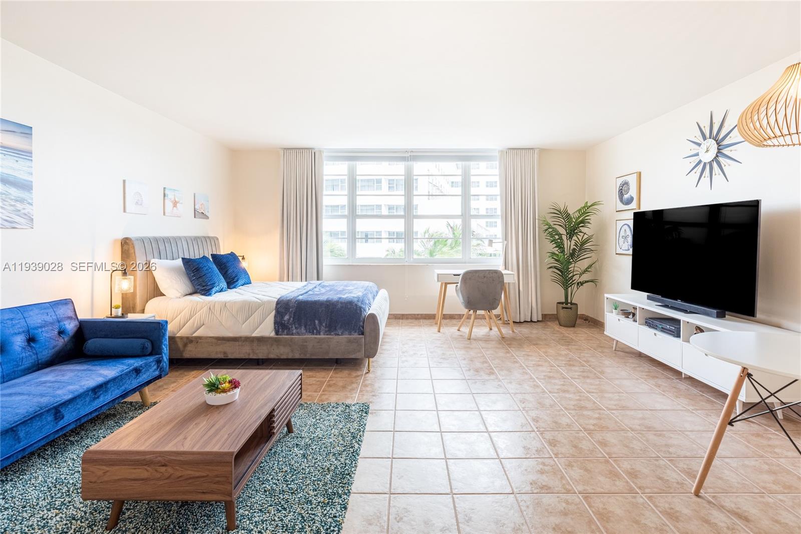 A studio apartment features a bed, blue sofa, television, desk, and tile flooring — 100 Lincoln Rd # 431, Miami Beach FL 33139, MIAMI BEACH, FL