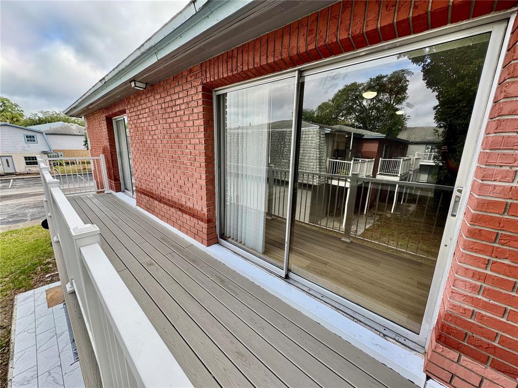 A balcony with light-colored composite decking and a white railing runs along a brick wall — 3045 AARON BURR AVENUE UNIT 12D, WINTER PARK, FL
