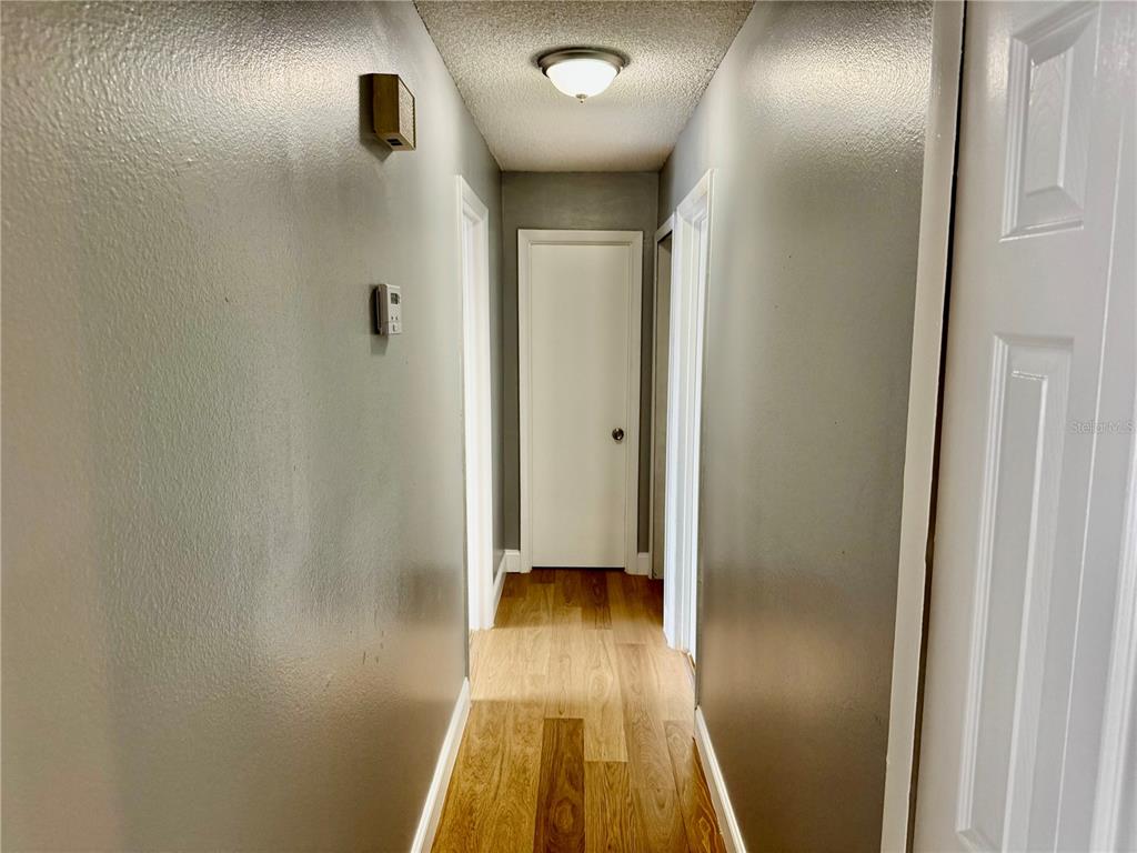 A narrow hallway features gray walls, wood-look flooring, and white doors under a ceiling light — 3045 AARON BURR AVENUE UNIT 12D, WINTER PARK, FL