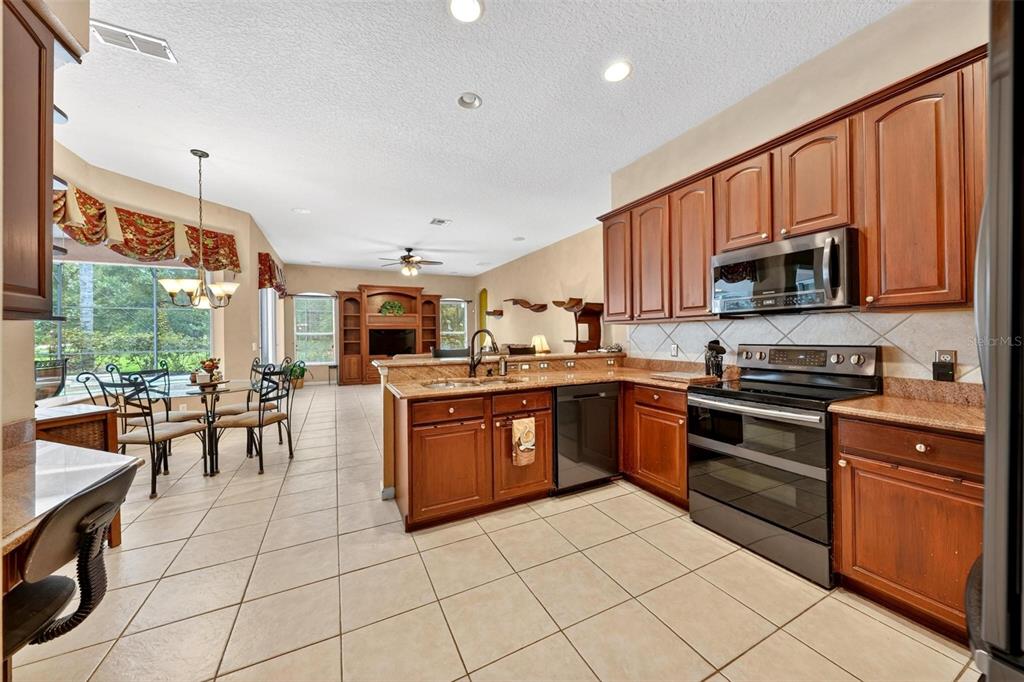 A kitchen with wood cabinets and granite countertops opens to a dining area and living room — 4385 SEA ROCK COURT, APOPKA, FL
