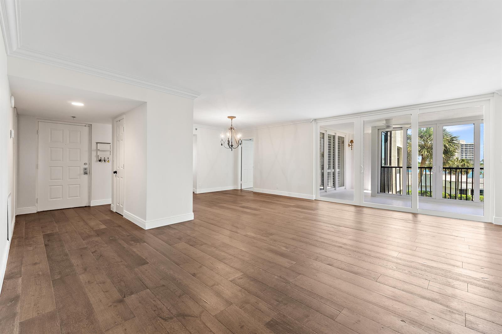 An empty living area with wood floors, a chandelier, and sliding glass doors to a balcony — 19800 Sandpointe Bay Drive # 305, Tequesta FL 33469, TEQUESTA, FL