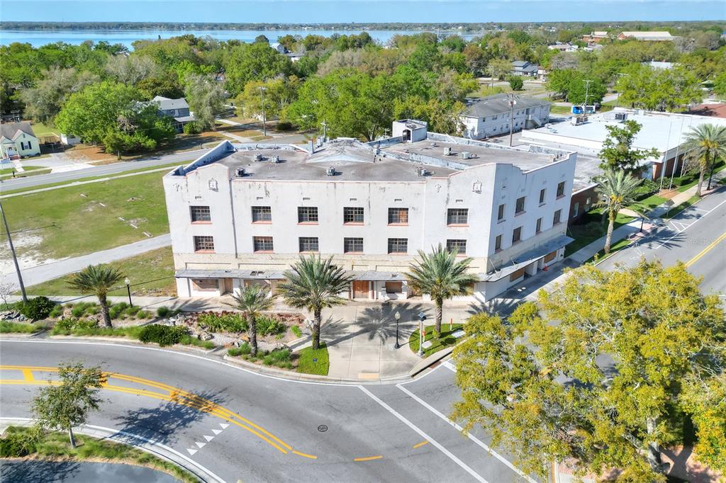 An aerial view of a three-story, light-colored commercial building situated at a street corner — 206 PILAKLAKAHA AVENUE, AUBURNDALE, FL