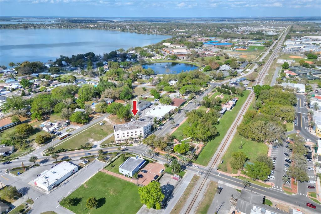 An aerial view shows a multi-story building marked with a red arrow near a lake — 206 PILAKLAKAHA AVENUE, AUBURNDALE, FL