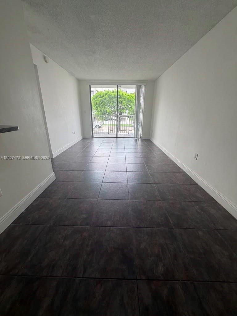 A long, narrow room features white walls, dark tiled flooring, and a sliding glass door — 8185 NW 7th St # 218, Miami FL 33126, MIAMI, FL