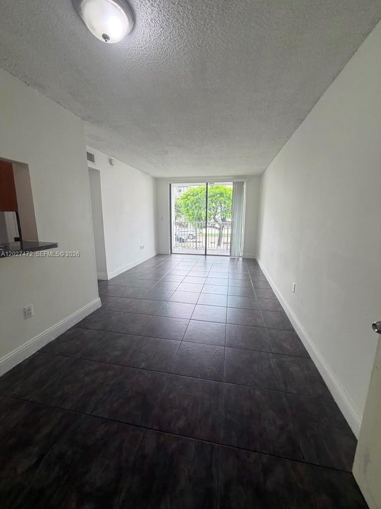 A living room with dark tile flooring and a sliding glass door leading to a balcony — 8185 NW 7th St # 218, Miami FL 33126, MIAMI, FL
