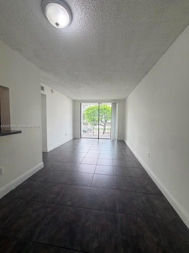 An empty room features dark tile flooring, white walls, and a sliding glass balcony door — 8185 NW 7th St # 218, Miami FL 33126, MIAMI, FL