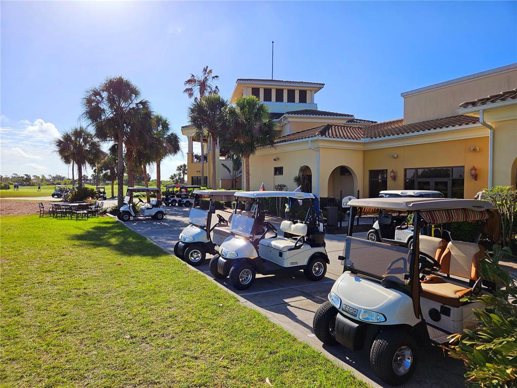 A row of golf carts is parked on a paved path outside a clubhouse building — 209 MESTRE PLACE, NORTH VENICE, FL
