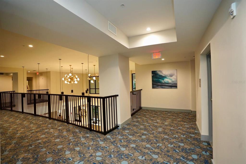 A carpeted hallway overlooks a lower level with a chandelier and black metal railings — 15695 GROVE RESORT AVENUE UNIT 4303, WINTER GARDEN, FL