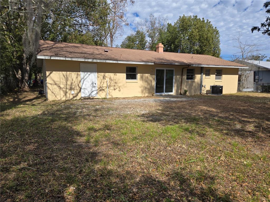 The rear exterior of a single-story yellow house features a sliding glass door and windows — 2204 SW 6TH STREET, OCALA, FL