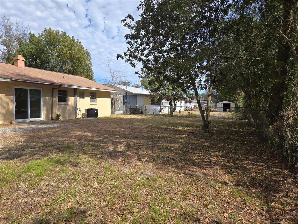 A backyard view of a tan house with a sliding glass door and a shed — 2204 SW 6TH STREET, OCALA, FL