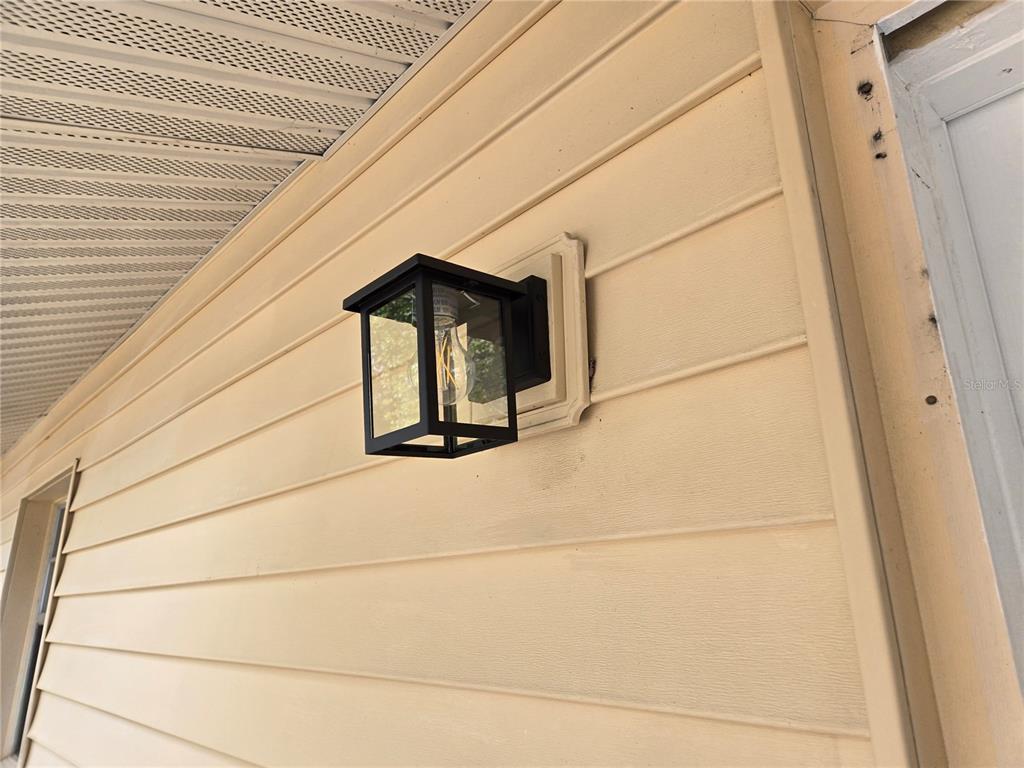 A black outdoor wall lantern is mounted on the beige vinyl siding of a house — 2204 SW 6TH STREET, OCALA, FL