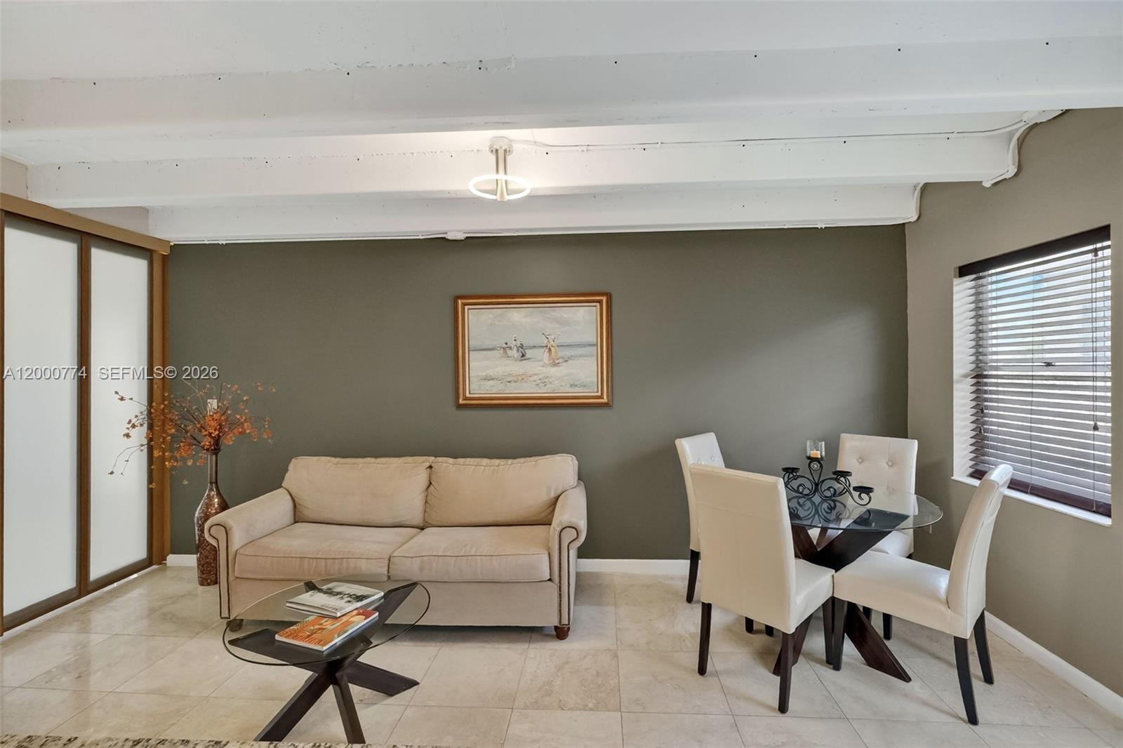 A living and dining area features a beige sofa, glass table, and white ceiling beams — 1519 Drexel Ave, Miami Beach FL 33139, MIAMI BEACH, FL