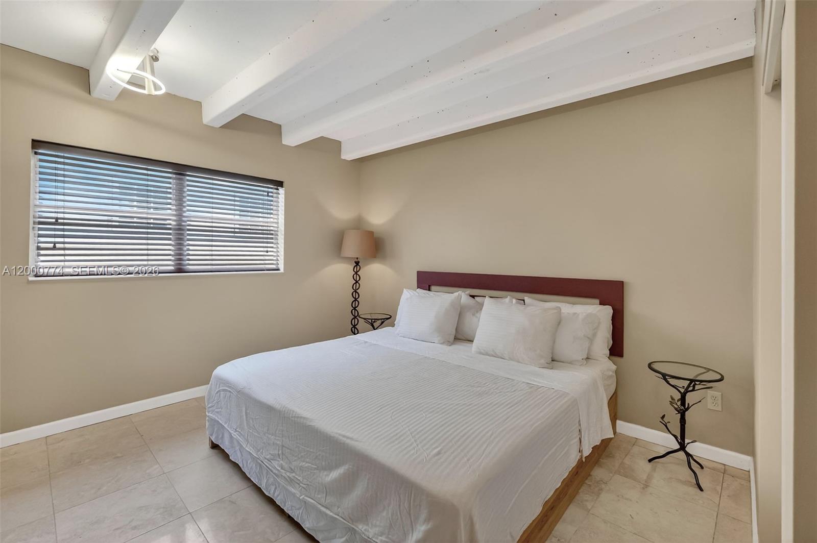 A bedroom features a bed with white bedding, a dark headboard, and exposed ceiling beams — 1519 Drexel Ave, Miami Beach FL 33139, MIAMI BEACH, FL