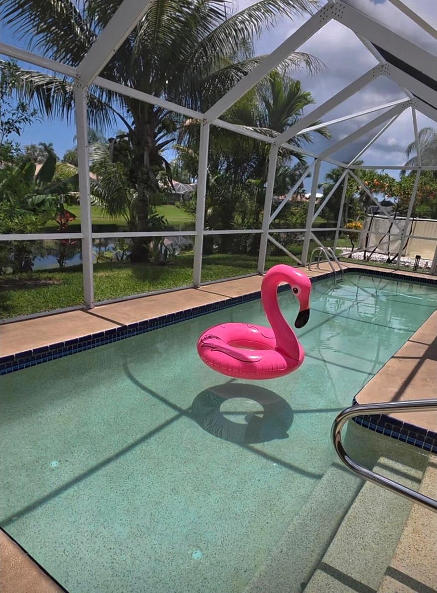 A pink flamingo pool float sits in a screened-in swimming pool overlooking a grassy yard — 9352 Cascade Court, Boynton Beach FL 33437, BOYNTON BEACH, FL