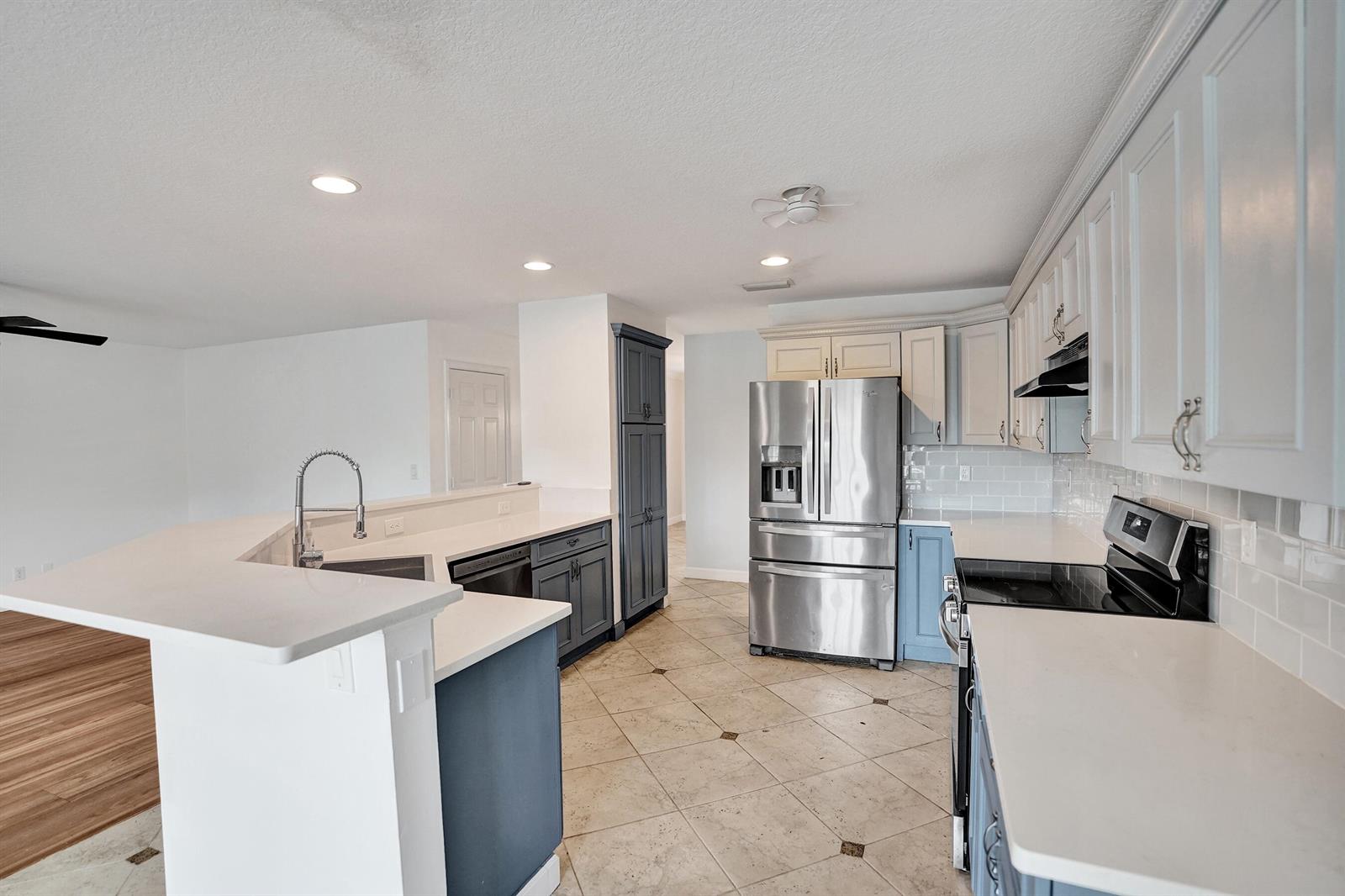 A kitchen features white countertops, blue and white cabinetry, stainless steel appliances, and tile flooring — 9352 Cascade Court, Boynton Beach FL 33437, BOYNTON BEACH, FL
