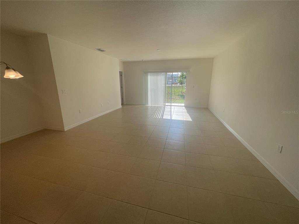 An empty living room features light-colored tile flooring, white walls, and sliding glass patio doors — 2007 HANDSOME HILL LANE, DAVENPORT, FL