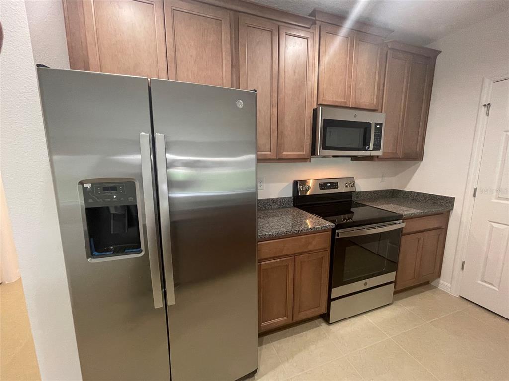 A kitchen features stainless steel appliances, wood cabinets, and granite countertops — 2007 HANDSOME HILL LANE, DAVENPORT, FL