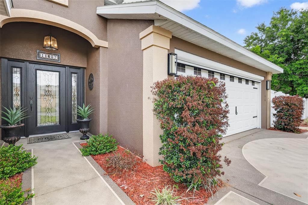 The exterior of a house features a dark front door, a garage, and landscaped bushes — 11637 LAKE DRIVE, LEESBURG, FL