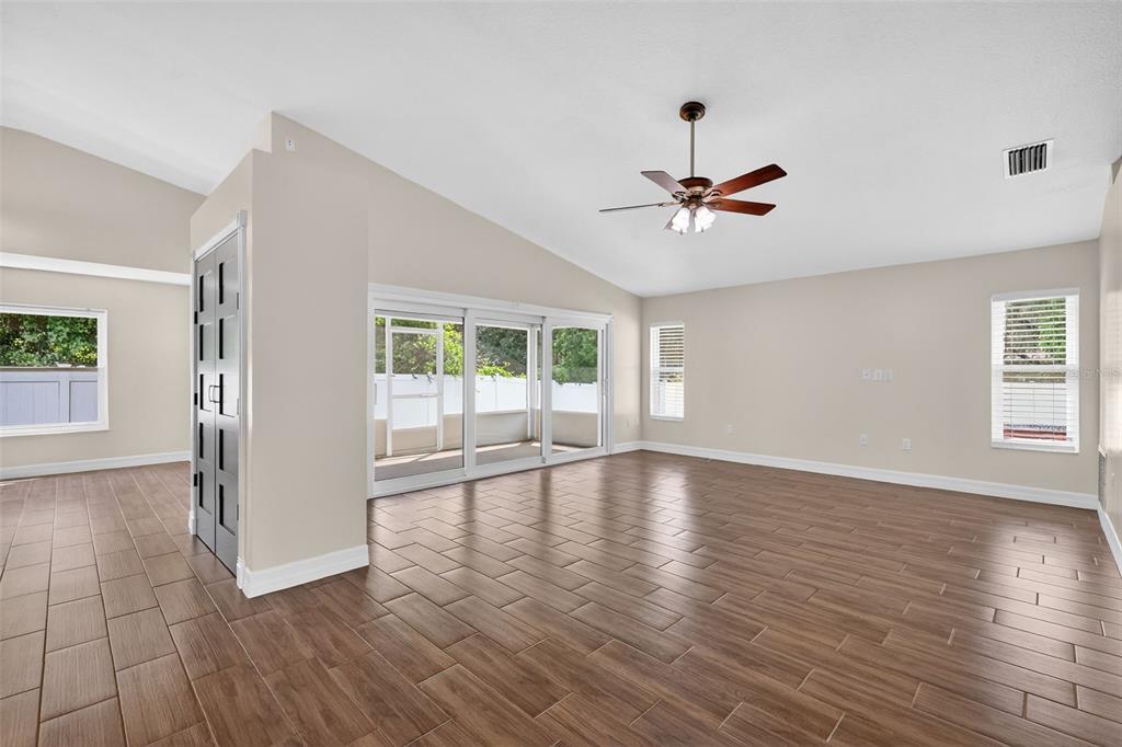 A spacious living room features wood-look tile flooring, a vaulted ceiling, and sliding glass doors — 11637 LAKE DRIVE, LEESBURG, FL