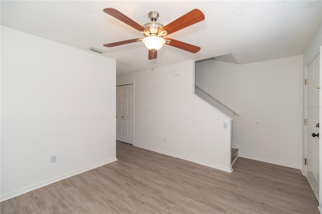 A room with light wood-look flooring, white walls, a ceiling fan, and a staircase — 344 CERVANTES DRIVE, KISSIMMEE, FL