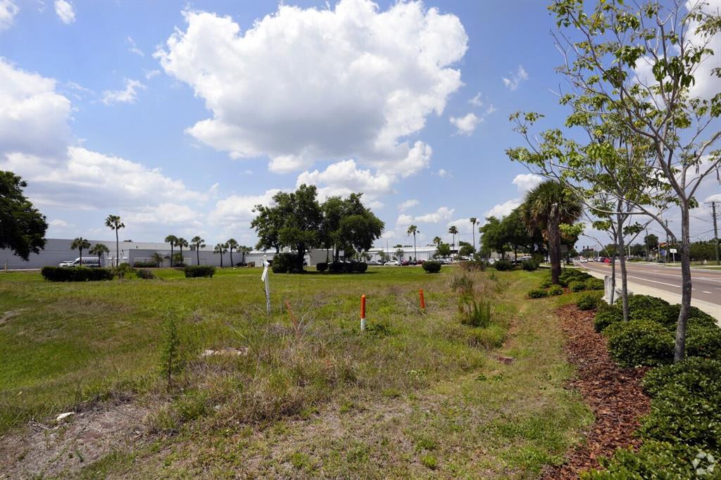 A vacant, grassy lot sits adjacent to a paved road with trees and distant buildings — 4201 W CREST AVENUE, TAMPA, FL