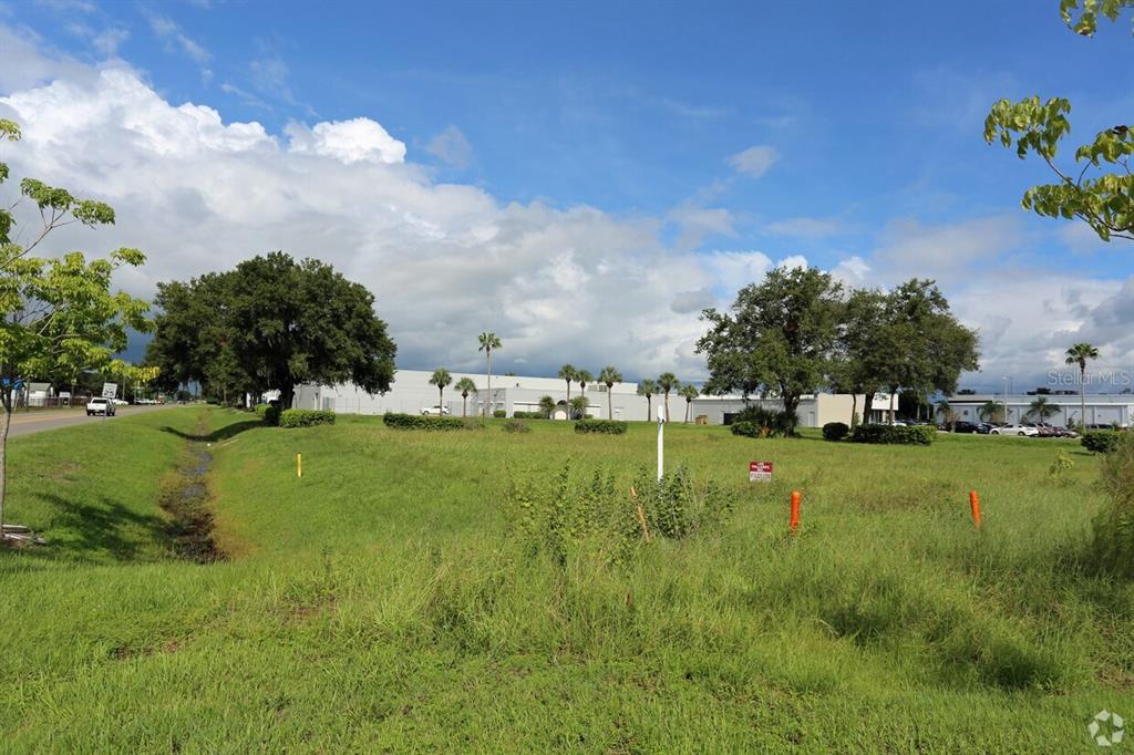 A grassy, undeveloped lot with scattered trees and a drainage ditch near a commercial building — 4201 W CREST AVENUE, TAMPA, FL