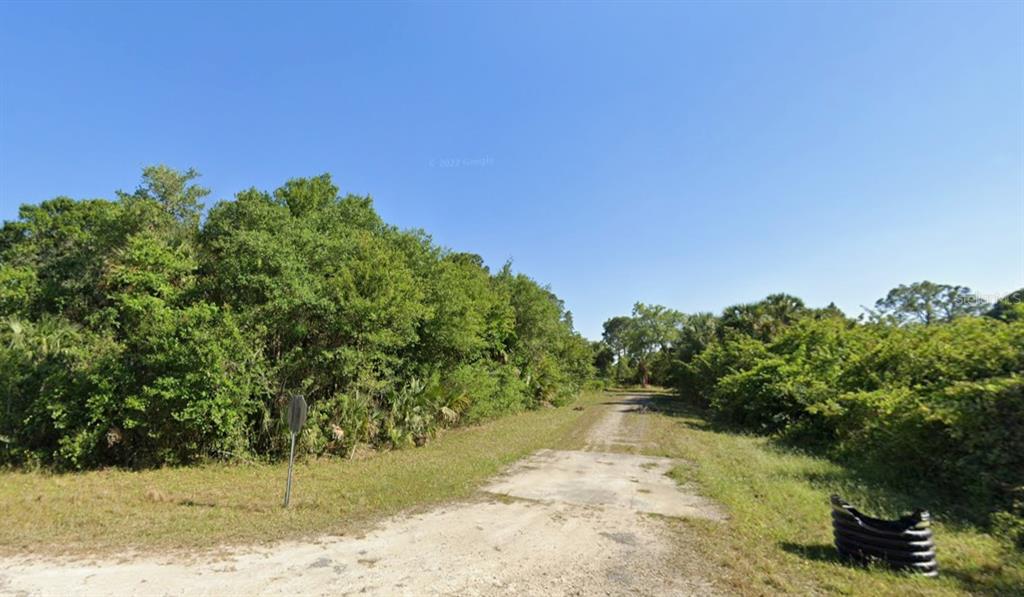 A dirt path leads into a dense, wooded area under a clear blue sky — 4702 VERA AVENUE N, LEHIGH ACRES, FL