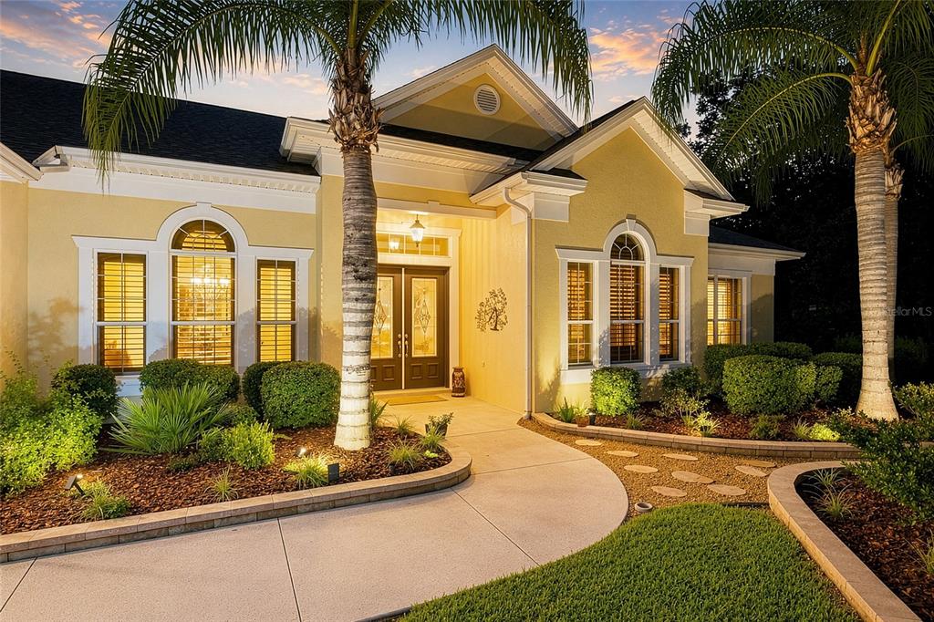 A yellow house with a concrete walkway, palm trees, and arched windows at dusk — 2063 LAKE RIDGE DRIVE, THE VILLAGES, FL