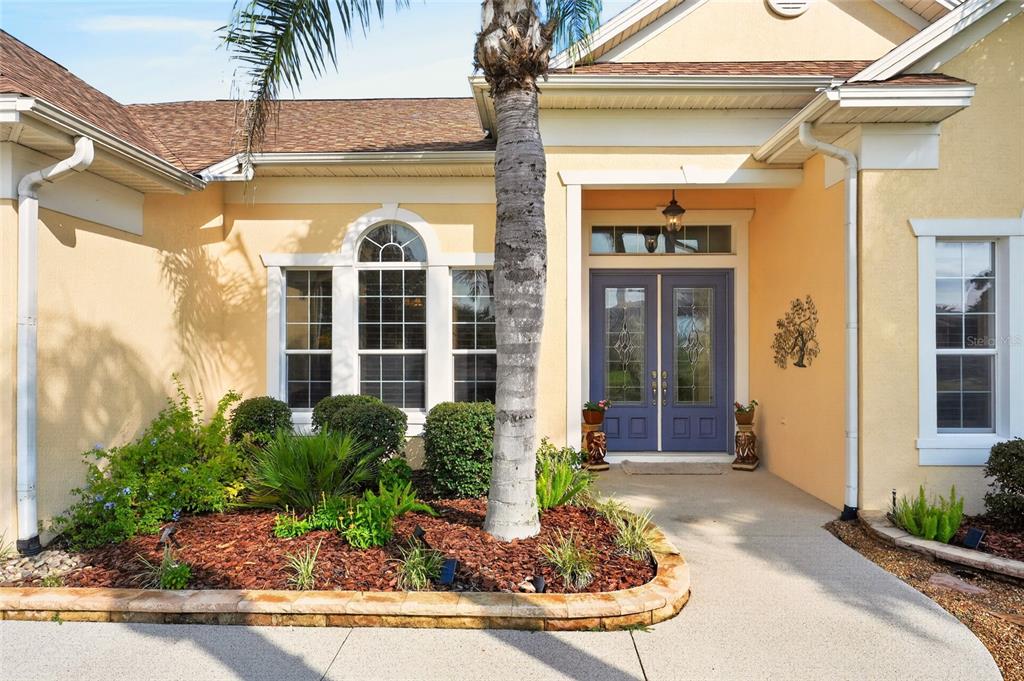 The exterior of a house features a tan stucco facade, a palm tree, and purple double doors — 2063 LAKE RIDGE DRIVE, THE VILLAGES, FL