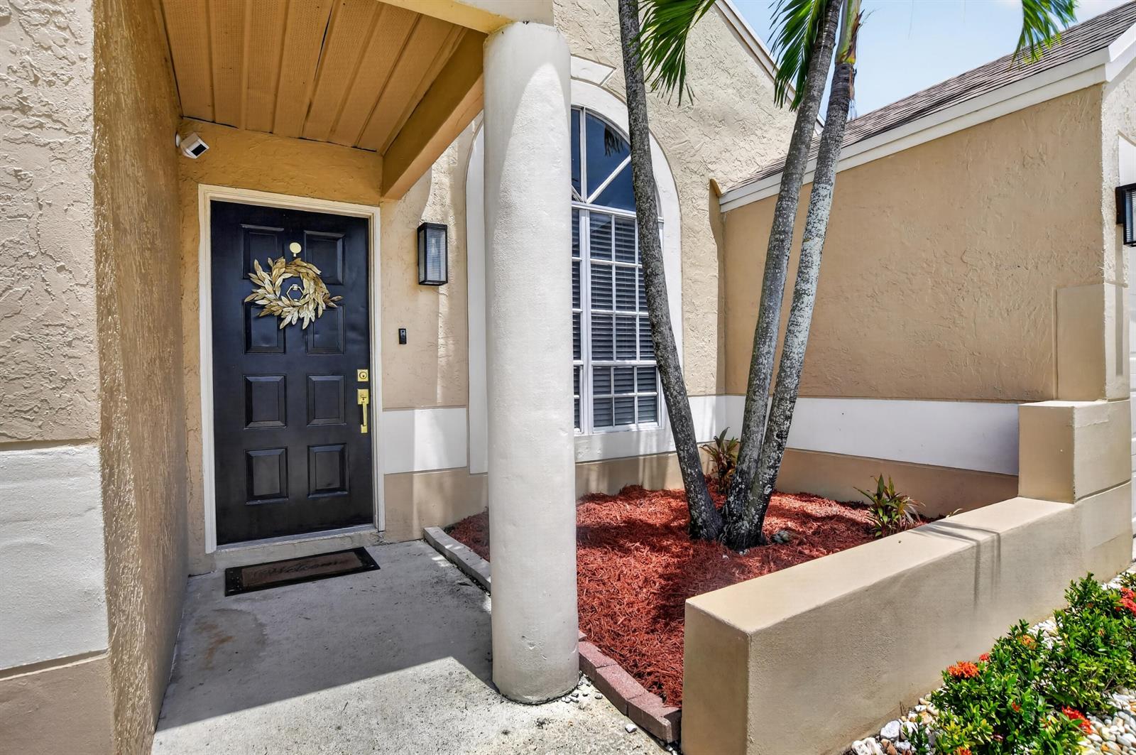 An exterior view of a home entrance featuring a black door, column, and palm tree — 23172 Bentley Place, Boca Raton FL 33433, BOCA RATON, FL