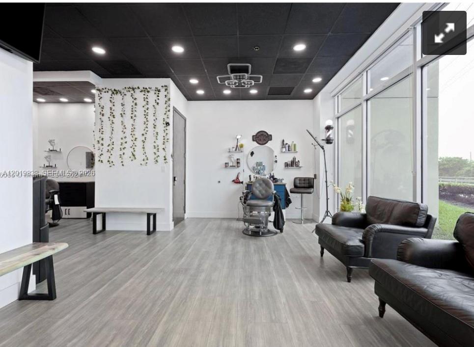 A modern barbershop interior featuring a black drop ceiling, gray wood flooring, and leather seating — 2300 W 84th St, Hialeah FL 33016, HIALEAH, FL