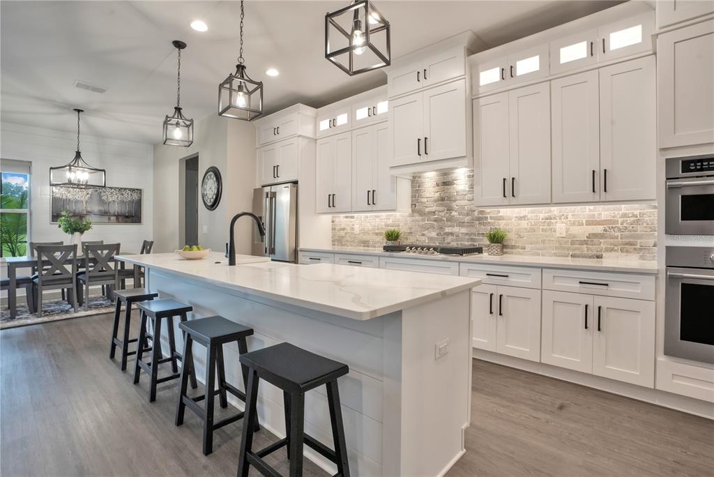 A modern kitchen features white cabinetry, a large island with bar seating, and brick backsplash — 440 PALMA CEIA ROAD, WINTER HAVEN, FL