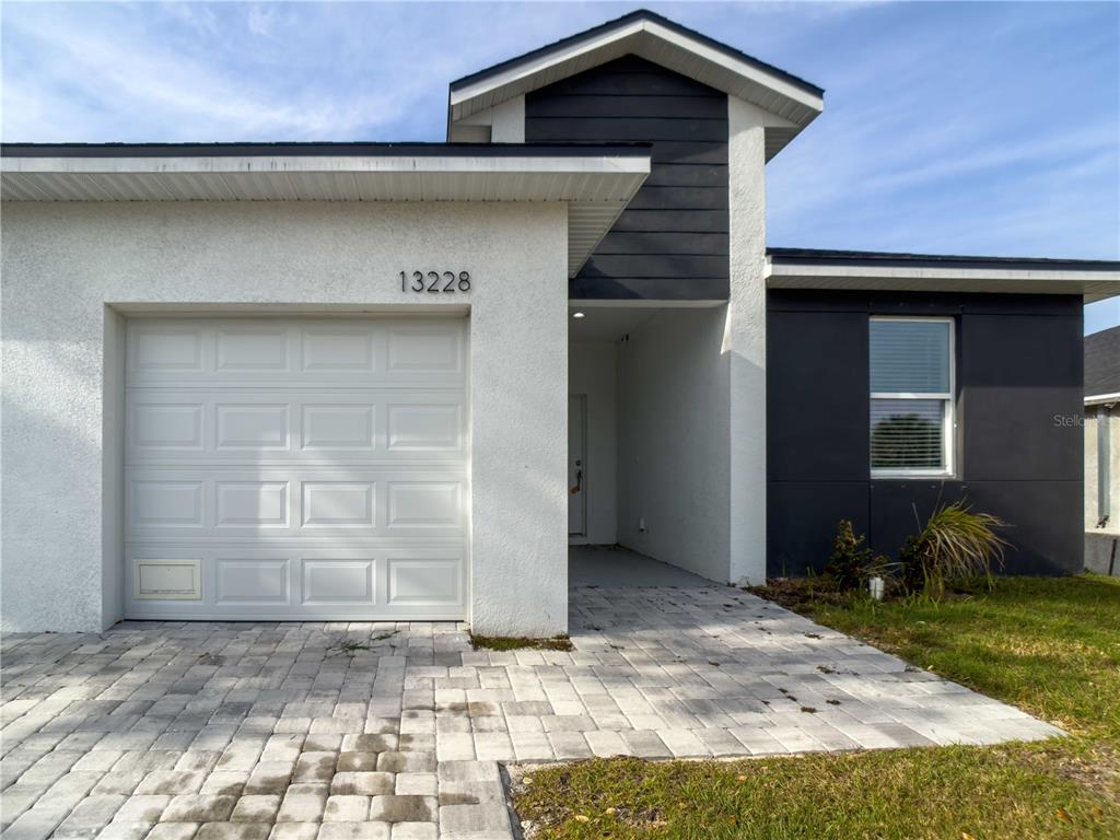 A modern house exterior features a white garage, a dark accent wall, and paver driveway — 13228 BLYTHEVILLE AVENUE AVENUE, PORT CHARLOTTE, FL