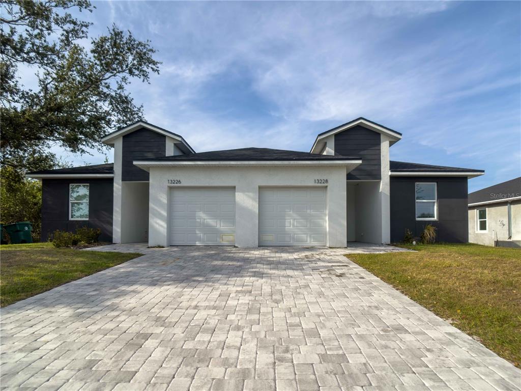 A duplex with white stucco, dark gray siding, two garage doors, and a paver driveway — 13228 BLYTHEVILLE AVENUE AVENUE, PORT CHARLOTTE, FL