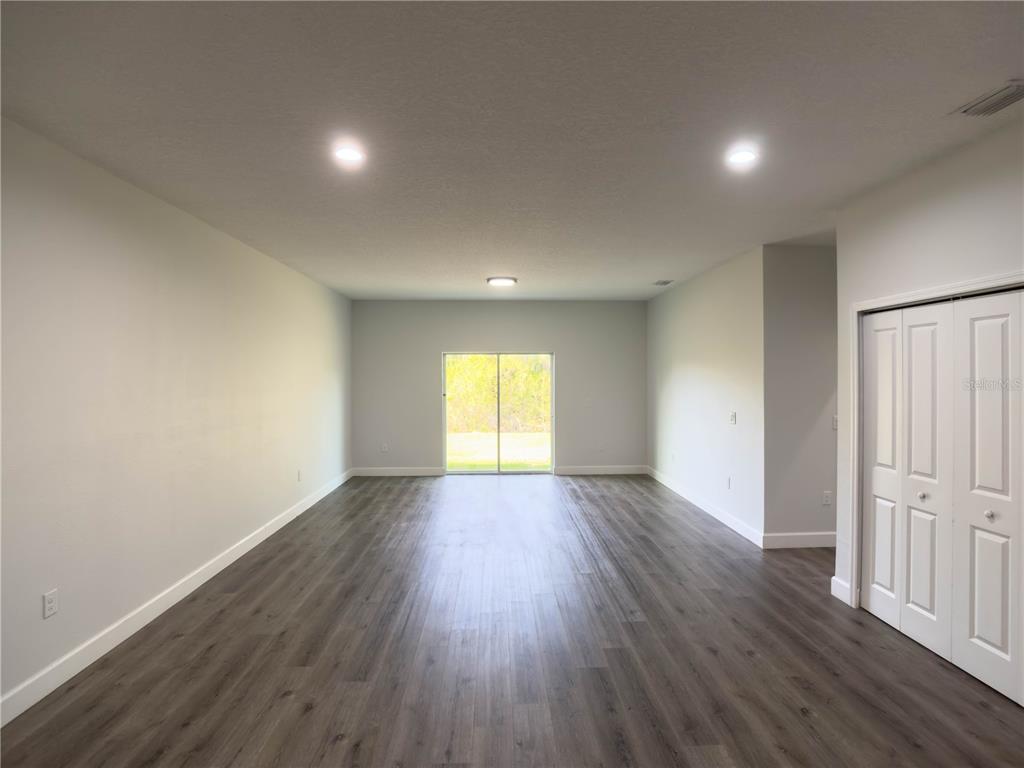 An empty room with gray wood-look flooring, white walls, recessed lighting, and sliding glass doors — 13228 BLYTHEVILLE AVENUE AVENUE, PORT CHARLOTTE, FL
