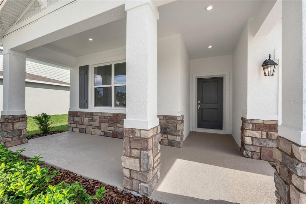 A covered front porch features stone-clad columns, a dark front door, and a single window — 1710 FLAG STREET, HAINES CITY, FL