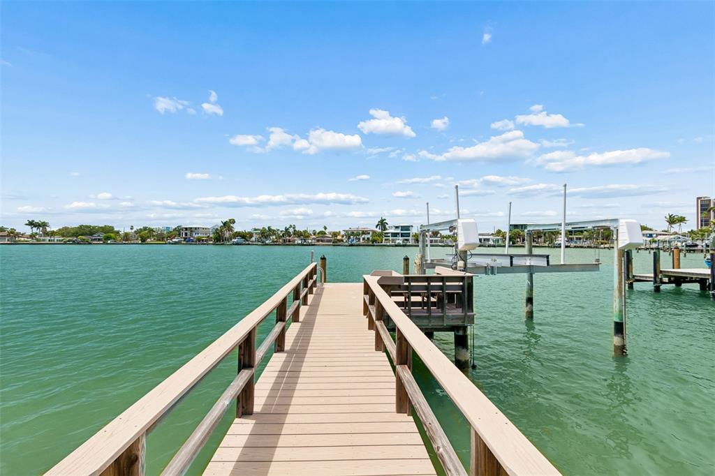 A wooden dock extends over calm water toward a distant shoreline under a blue sky — 10246 TARPON DRIVE, TREASURE ISLAND, FL