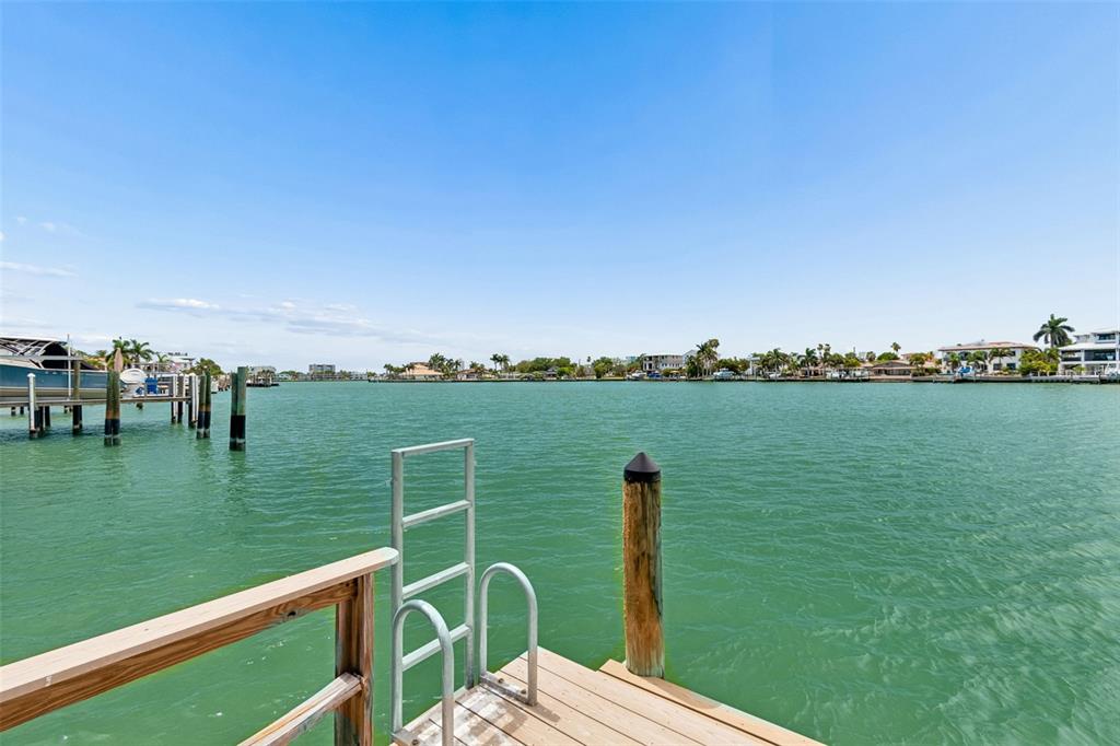 A wooden dock with a metal ladder extends into a calm, green waterway — 10246 TARPON DRIVE, TREASURE ISLAND, FL