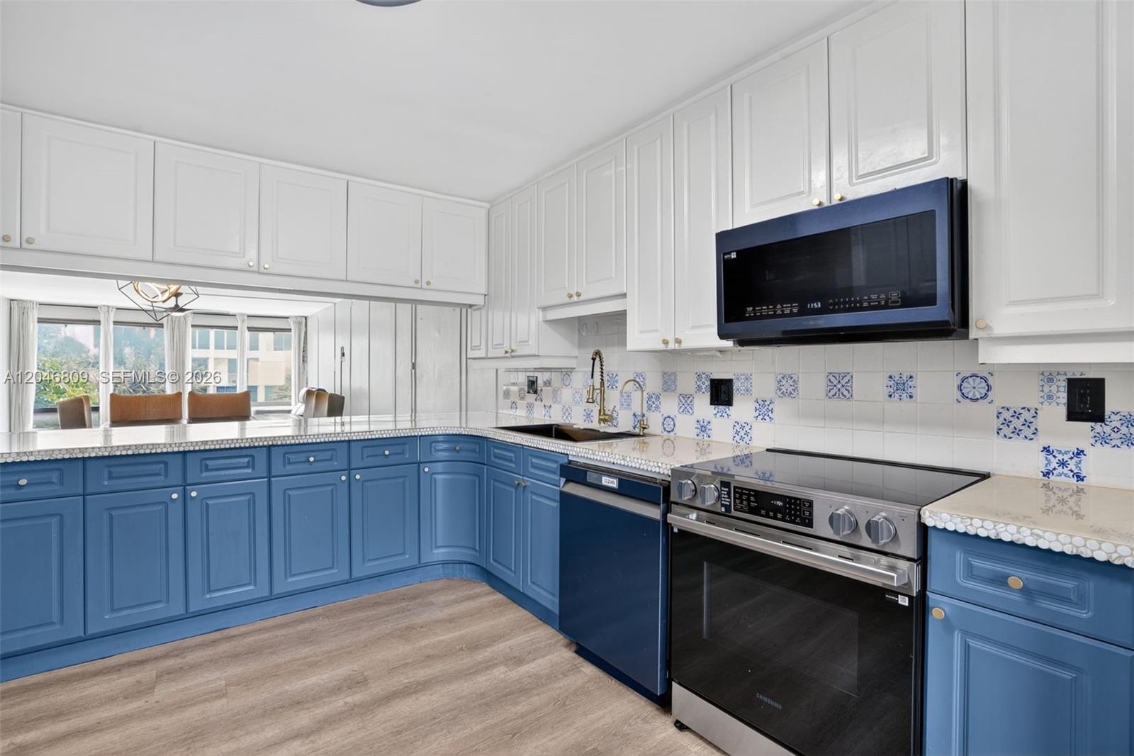 A kitchen features blue lower cabinets, white upper cabinets, patterned tile backsplash, and stainless appliances — 10240 Collins Ave # 207, Bal Harbour FL 33154, BAL HARBOUR, FL